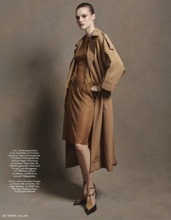 Model wearing a tan trench coat over a brown dress against a textured neutral background