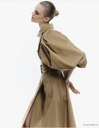 Model in profile wearing a belted camel coat with statement sleeves against a clean white background