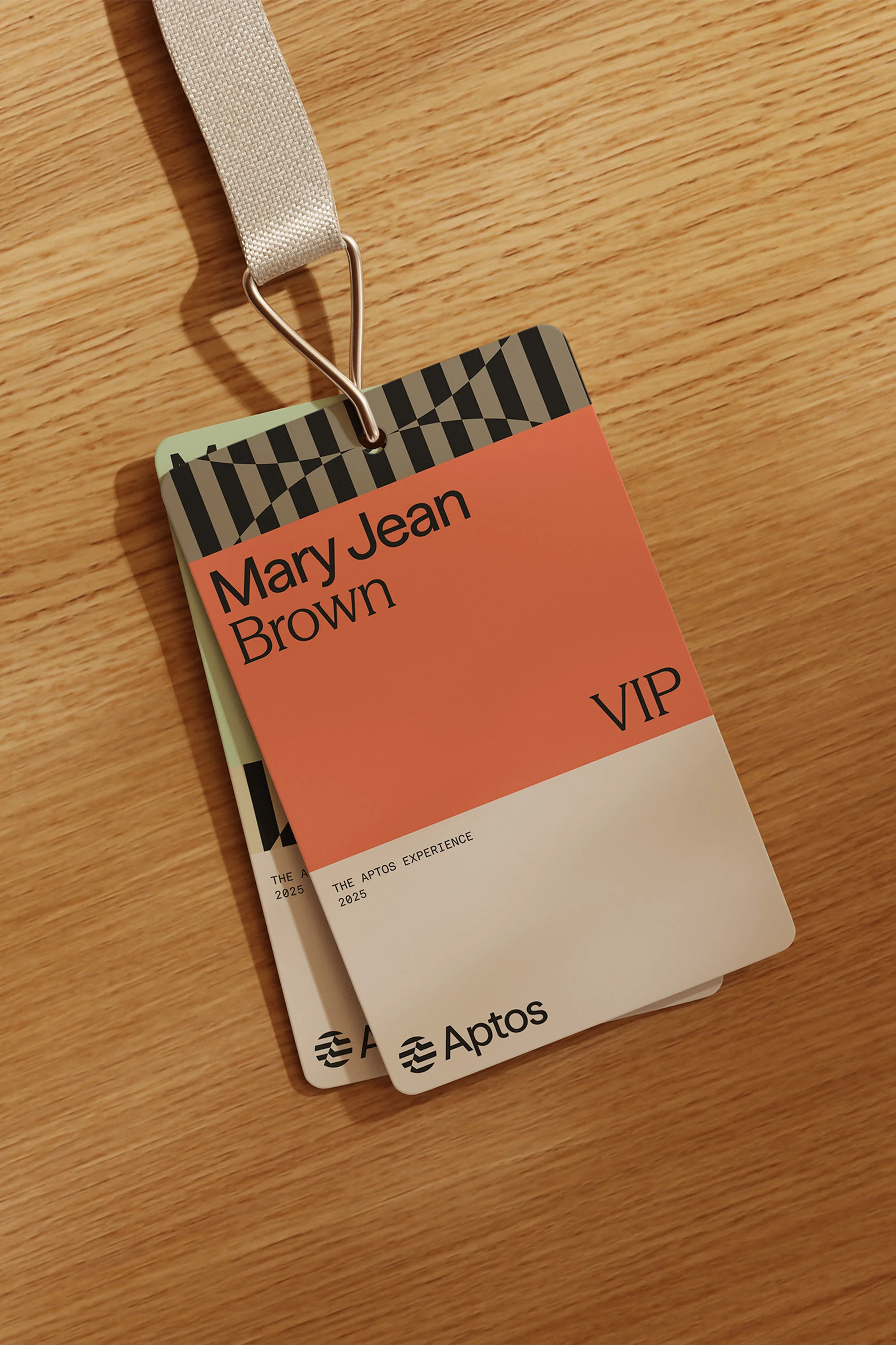 Close-up of two event badges with lanyards, featuring the Aptos logo, stacked on a light wood surface; one has a pink section with 'VIP'.