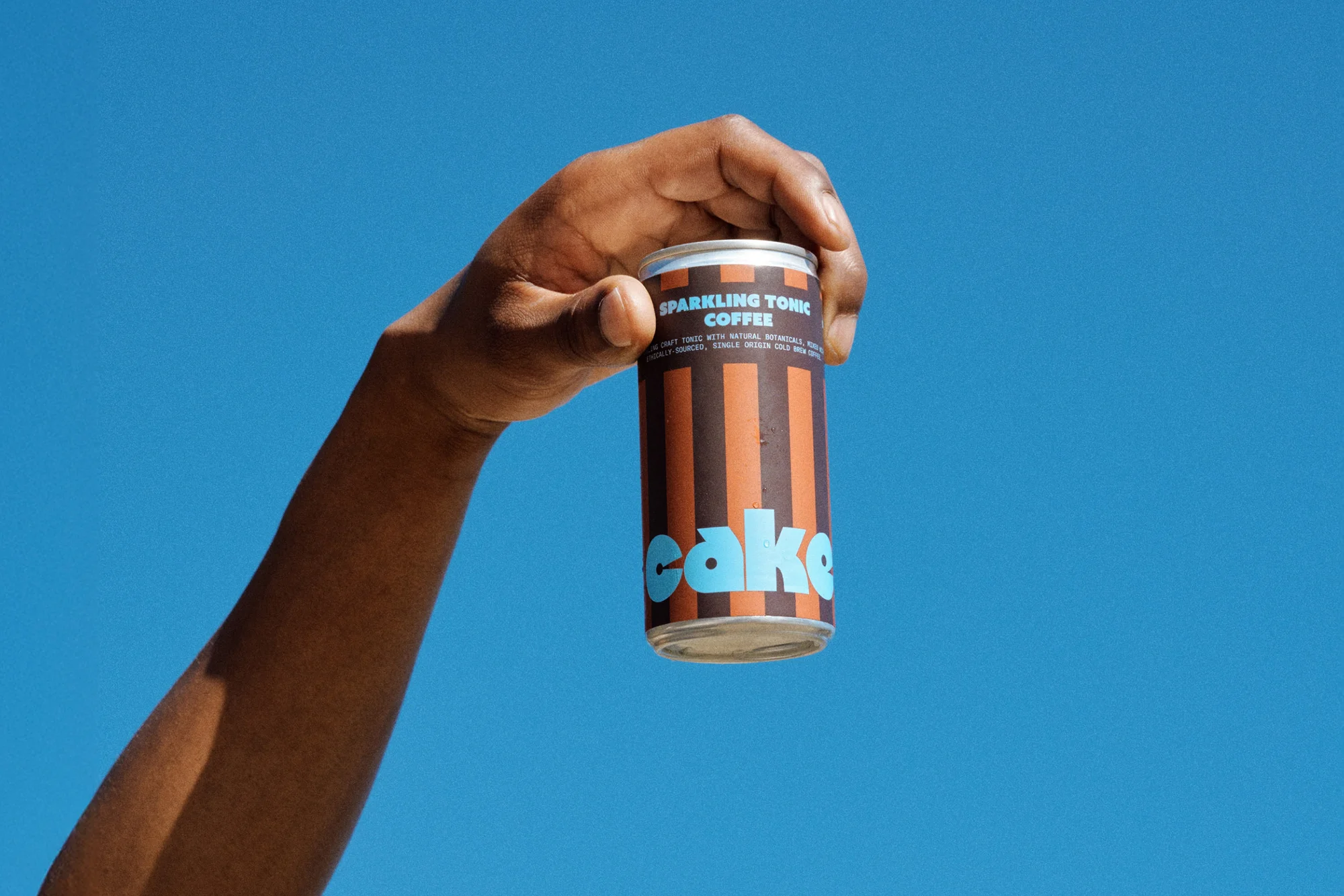 Close-up of a hand holding a can of sparkling tonic coffee against a bright blue sky, showcasing the product's branding and design.