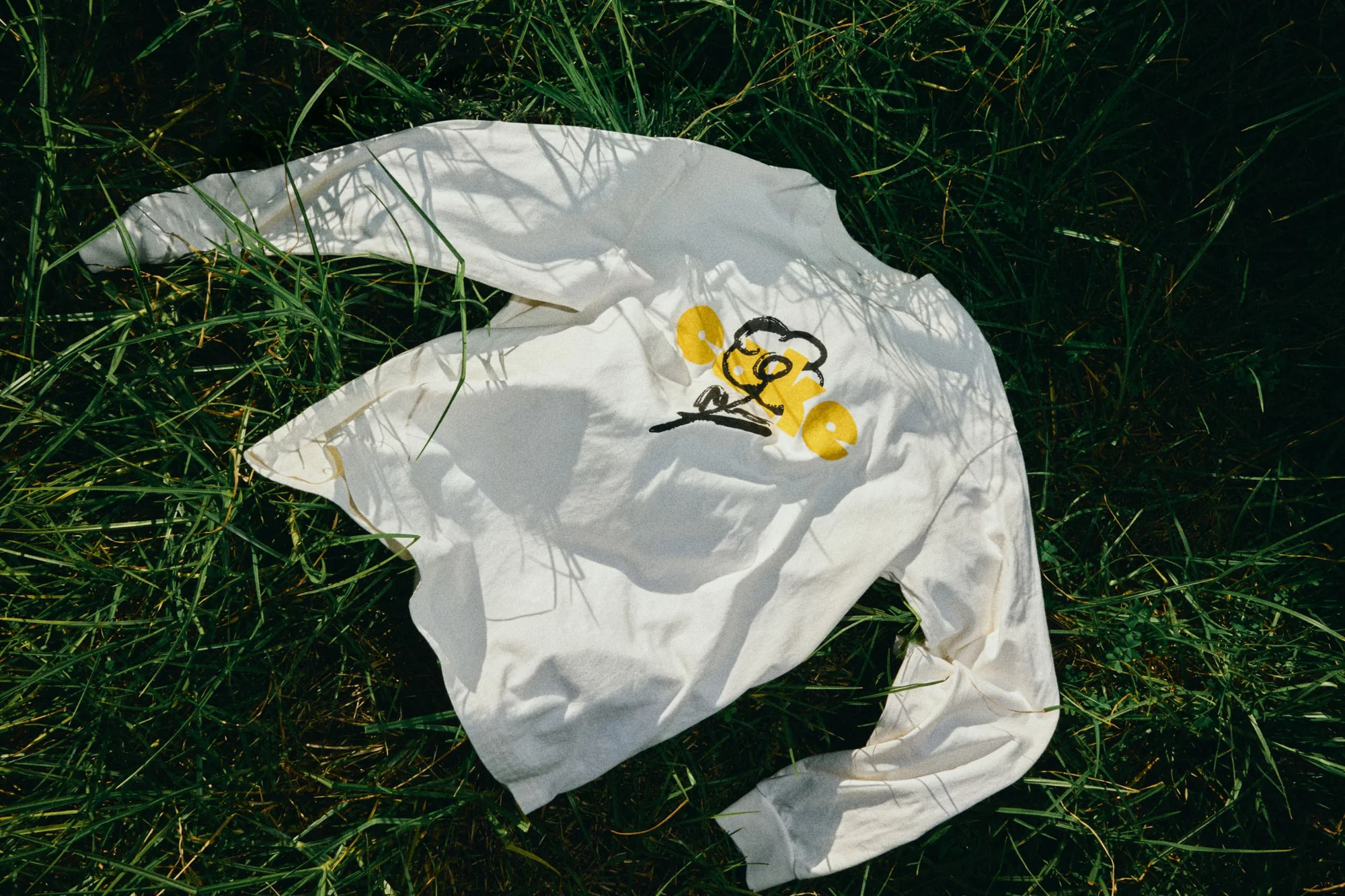 White long-sleeve shirt with graphic design on green grass backdrop, shot with natural light in an outdoor setting.