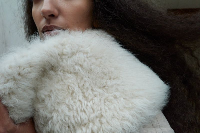 Close-up of a person with dark wavy hair wearing a textured white garment, focusing on texture and soft tones.