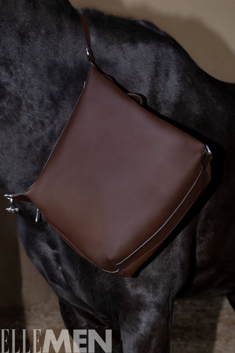 Brown leather shoulder bag draped over a black horse against a neutral background, shot in a studio setting. Ellemen logo visible.