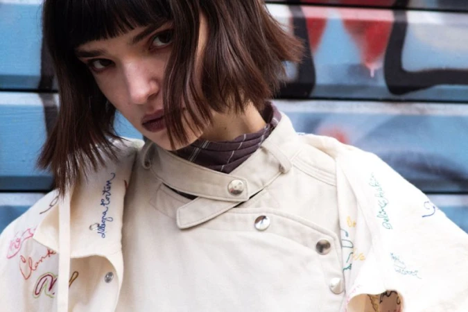 Model with dark bob haircut wearing an off-white embroidered jacket against a street backdrop