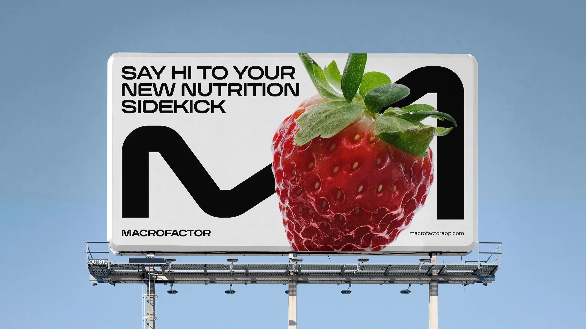 Billboard ad featuring a large strawberry and the MacroFactor app logo against a bright blue sky, advertising nutrition.
