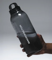 Hand holding a dark translucent water bottle with water droplets against a light grey studio background.