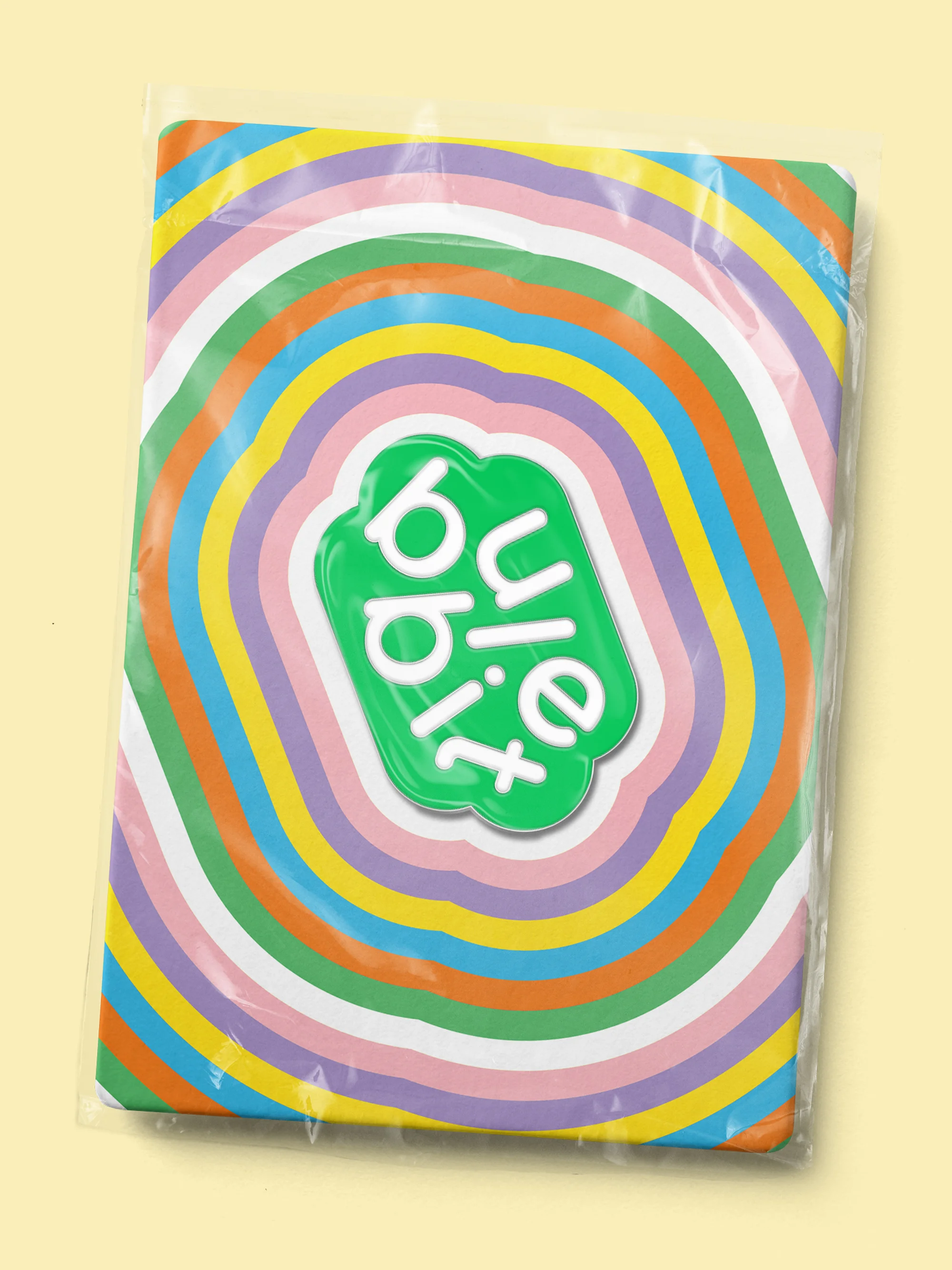 Overhead shot of Bule Bibit packaging with colorful concentric rings, encased in clear plastic, on a light yellow background.