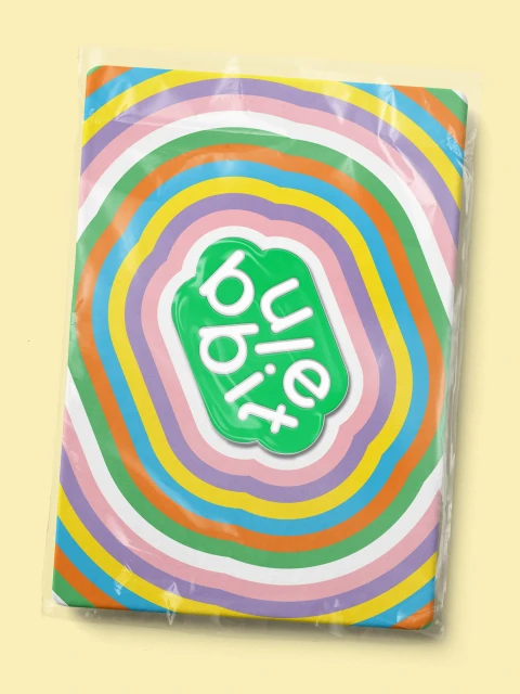 Overhead shot of Bule Bibit packaging with colorful concentric rings, encased in clear plastic, on a light yellow background.