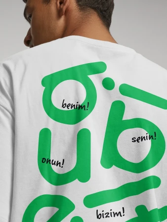 Man wearing a white t-shirt featuring large green typographic graphics and handwritten text on the back
