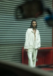 Model standing in cream textured jacket and trousers against a green roller shutter door with a red frame