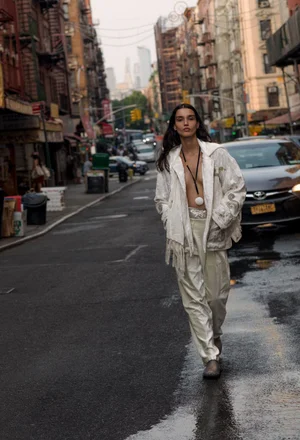 Model in white patterned jacket and trousers walking down an urban street