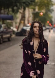 Model wearing a purple velvet shirt with shell embroidery walking on an urban city street outdoors.