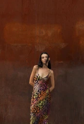 Model wearing a colourful patterned slip dress standing against a rusty metal wall for Forte_Forte AW24.