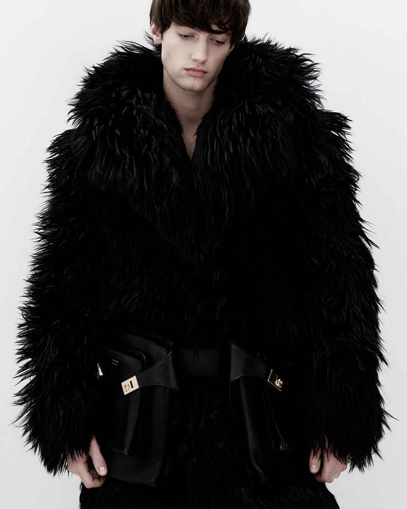 Fashionable adult male in black fur coat with bold pockets against a plain white backdrop in a studio setting. Editorial fashion shot.