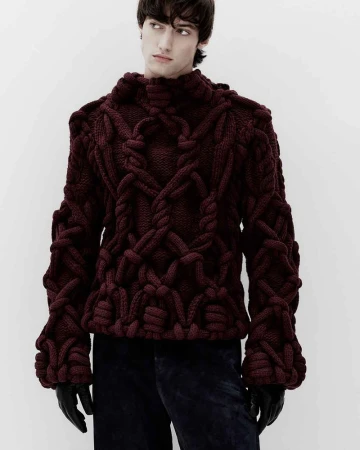 Model wearing a thick burgundy knotted knit sweater against a plain white background