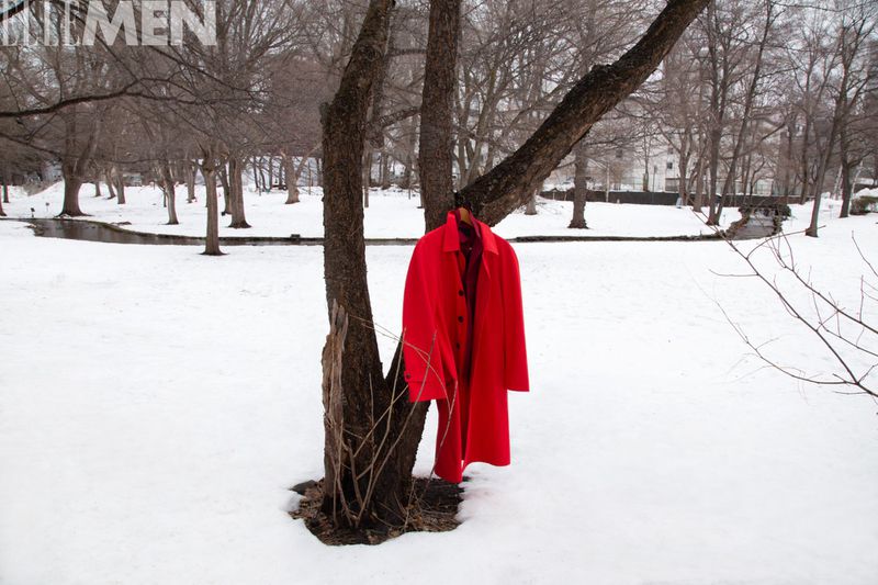 Red overcoat on a hanger displayed on a tree in a snowy landscape on an overcast day, creating a striking contrast against the white snow.