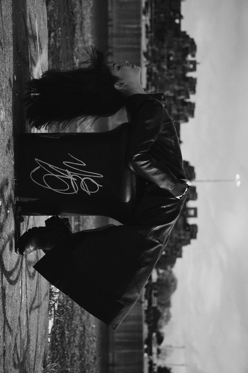 Monochrome fashion portrait of a person arching backward over a graffiti-covered bin outdoors.