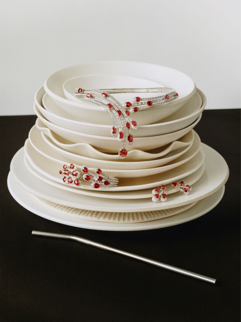 Elegant jewelry set featuring a necklace, bracelet, and ring adorned with red gems and diamonds, artfully arranged on a stack of white plates.