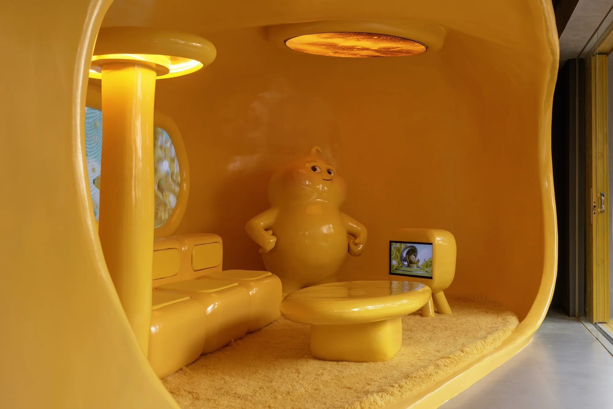 A yellow cartoon room with a couch, table, TV, and character statue, all bathed in a matching yellow hue, creates a surreal, playful scene.