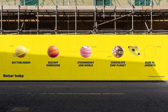 Whimsical outdoor billboard features planetary-themed artwork, advertising "Butter baby" with vibrant colors and playful design elements on a yellow background.