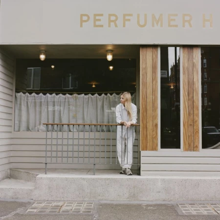 Woman in white shirt and pants leaning on railing outside Perfumer H storefront photographed by Linda Brownlee