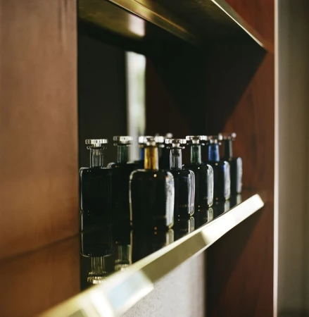 Row of dark glass perfume bottles with metallic caps on a reflective wooden shelf