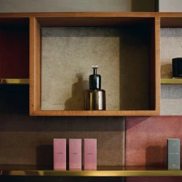 Amber glass perfume bottle on a wooden shelf above pink and green boxes for Perfumer H by Highsnobiety.
