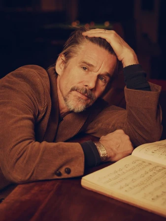 Close-up portrait of a middle-aged Caucasian man in a corduroy jacket, resting his head on his hand, with a music book nearby.