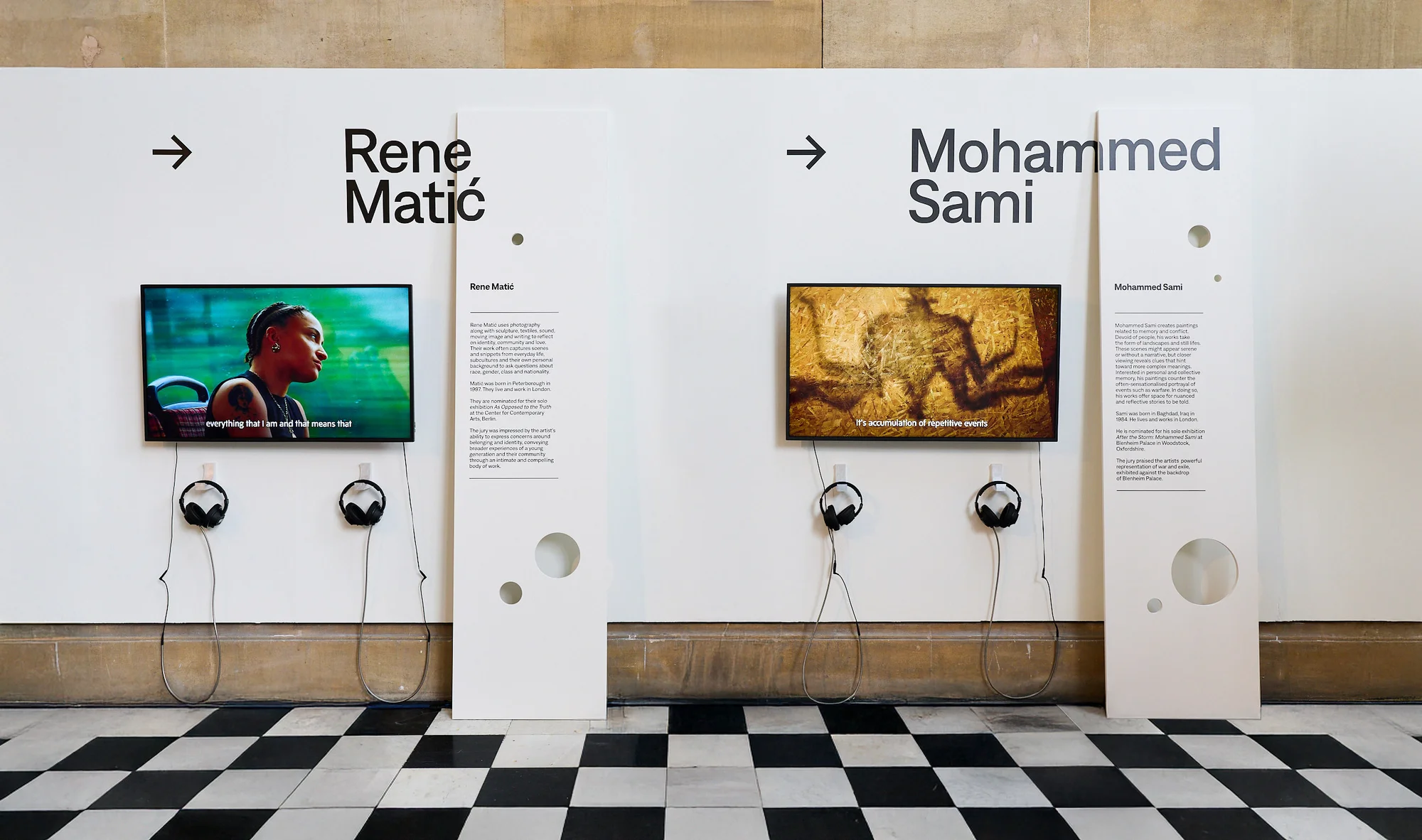 Art installation with video displays and headphones; checkerboard floor; exhibition showcases modern art.