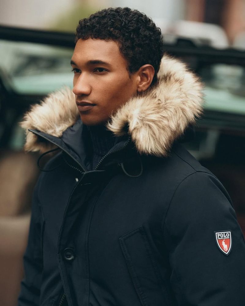 An adult male wears a Polo Ralph Lauren winter coat with fur trim while outside in an urban setting during the daytime.