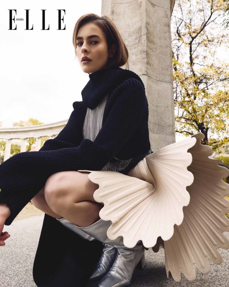Elle Arabia cover featuring a woman crouching with a fashion skirt, silver boots, and a black turtleneck sweater in an outdoor setting.