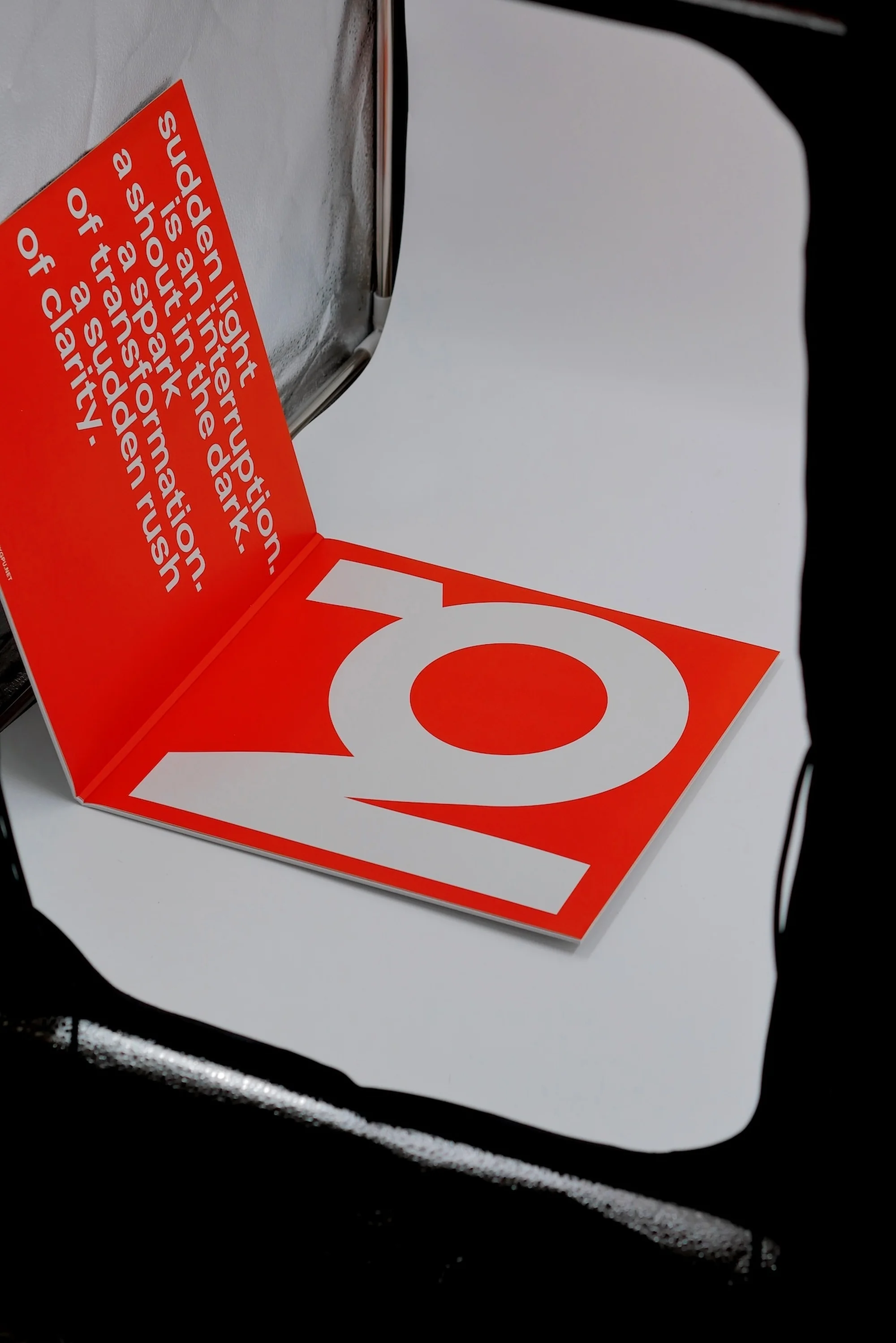 Graphic image featuring an opened red brochure with white text and a white letter 'Q' against a white and black background.