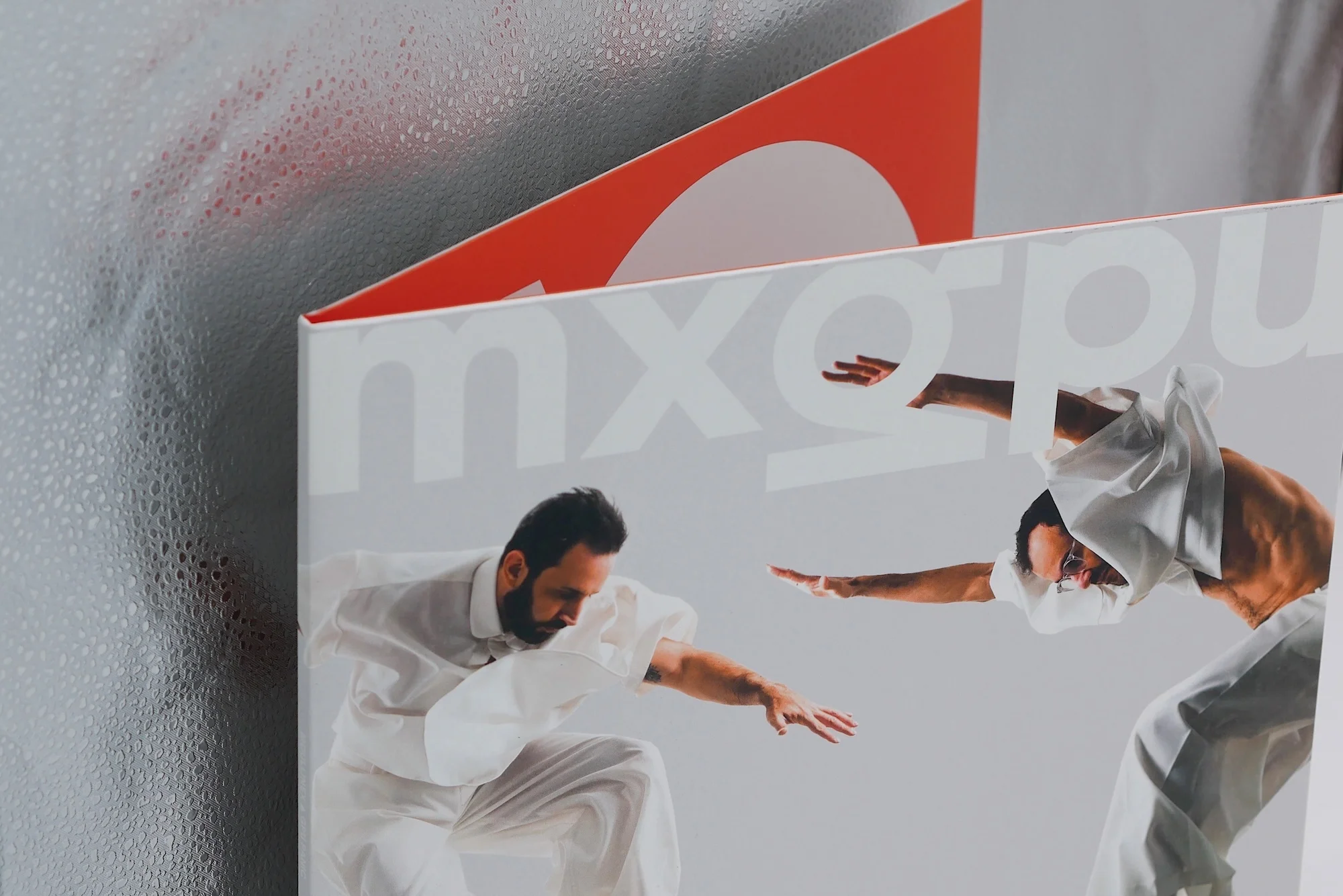 Two adult men in white outfits strike dynamic poses in a studio-style setting, creating a striking image with white and gray tones.