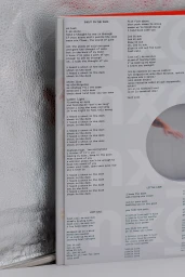 Close-up of a printed booklet page for MXGPU featuring typeset song lyrics and a circular window graphic.