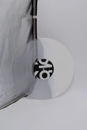 Clear vinyl record with a bold black and white center label leaning against a reflector panel in a studio setting.