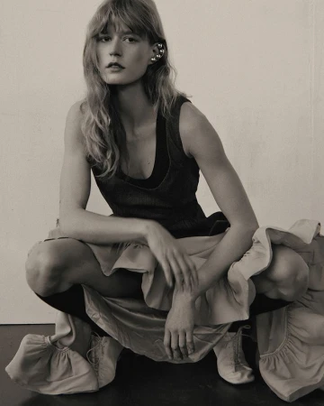 Model Sabina Ruegg crouching in a dark dress and ruffled skirt for Elle Serbia, photographed by Elena Kuznetsova.