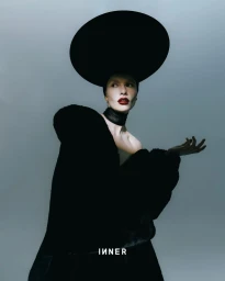 Model wearing a large black hat and dark coat against a gradient studio background for Inner Magazine.