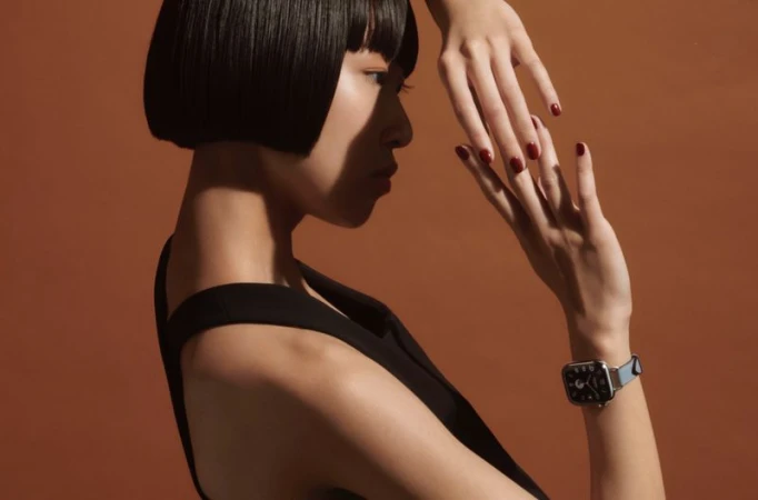 A profile shot of an Asian woman wearing a watch, accented by her hand position and short black hair, all set against a warm brown background.