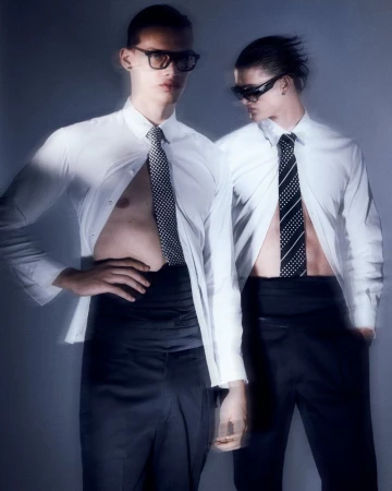 Two adult men pose indoors wearing white shirts, dark pants, ties, and sunglasses. One shirt is unbuttoned, revealing his chest.