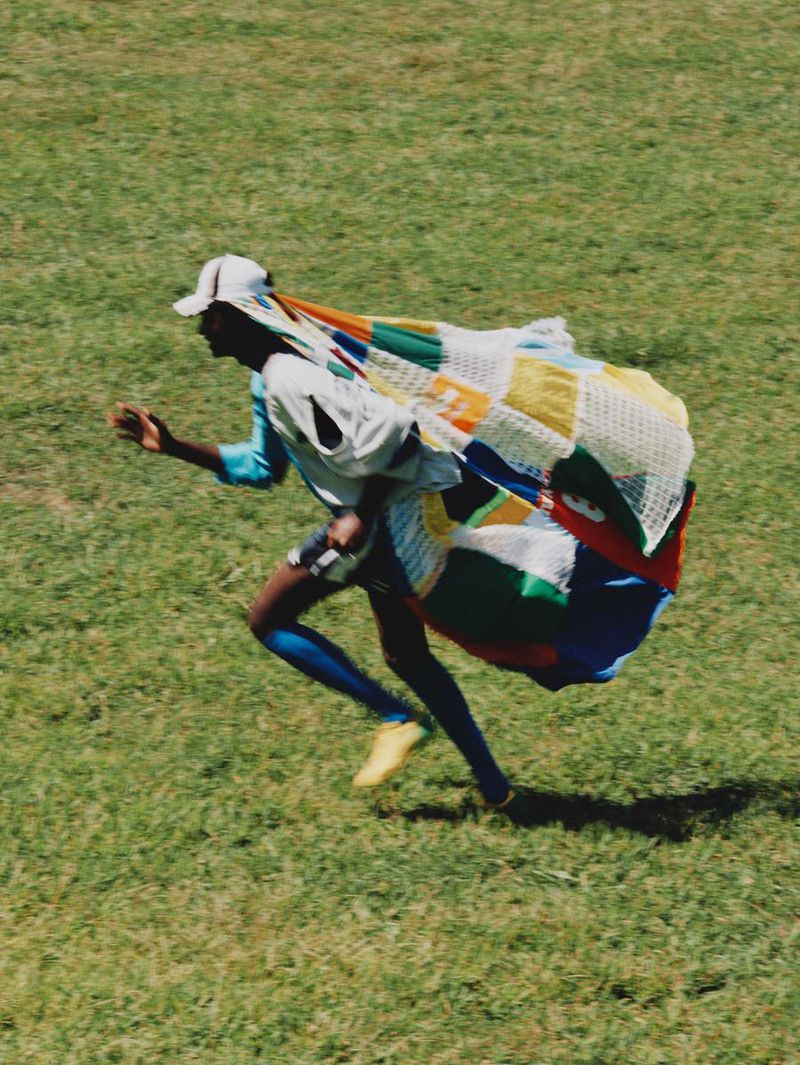 Athlete with colorful fabric running in a grassy field, wearing blue leggings and a white hat on a sunny day.