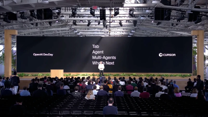 Audience at OpenAI DevDay event watches a speaker on stage in a large indoor space with a large screen displaying the event's theme.