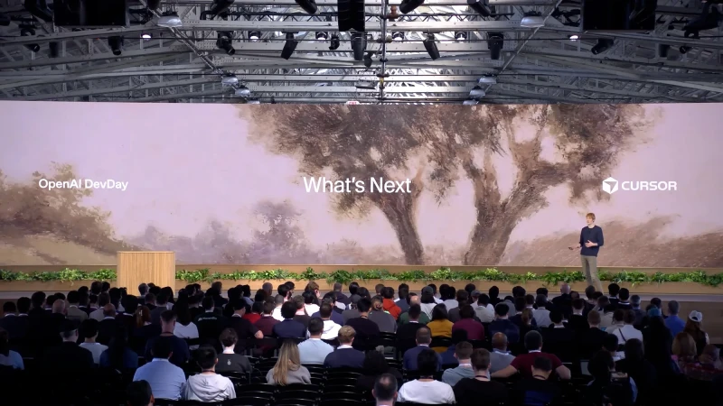 Audience watching a speaker at a tech conference with a screen displaying 'What's Next' and the Cursor logo on stage.