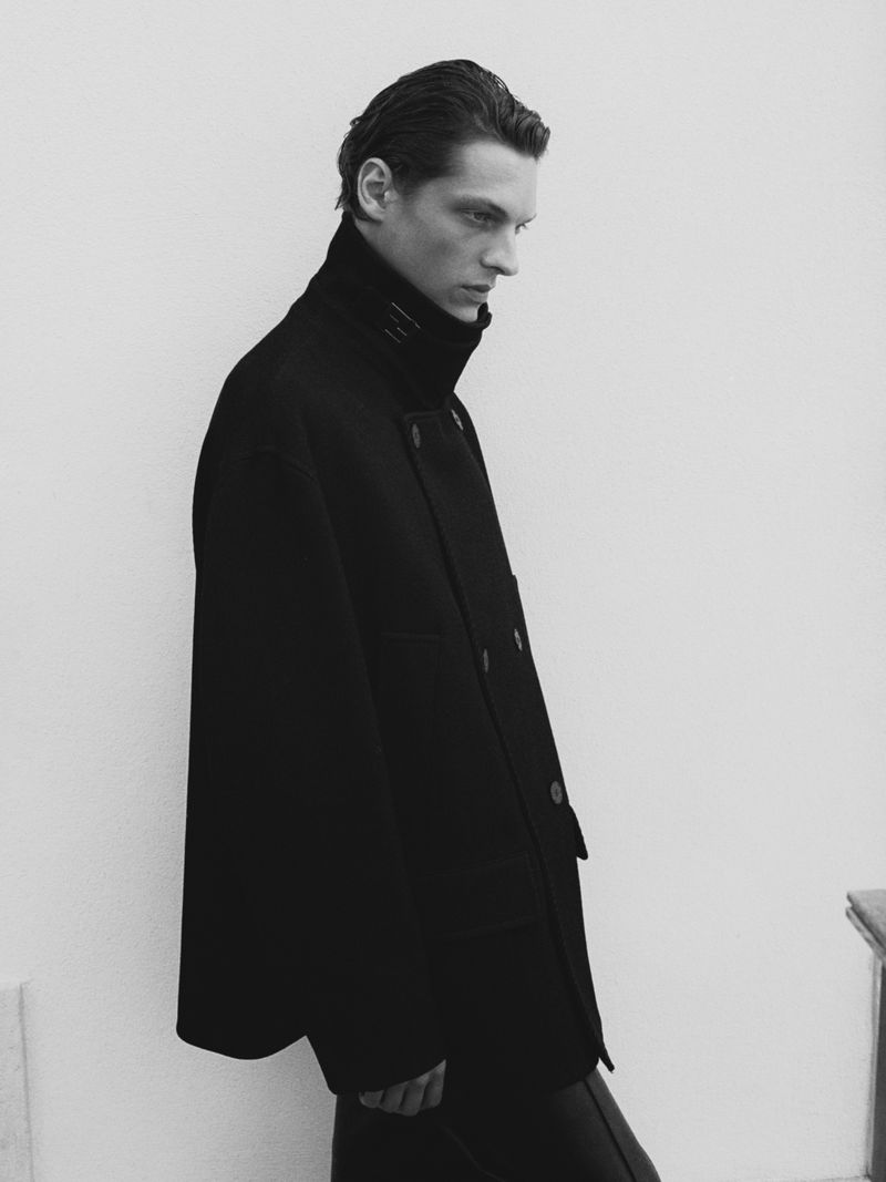 Monochrome fashion portrait of a man in a dark coat. High fashion photography with a neutral background, side view. Stylish men's outerwear.