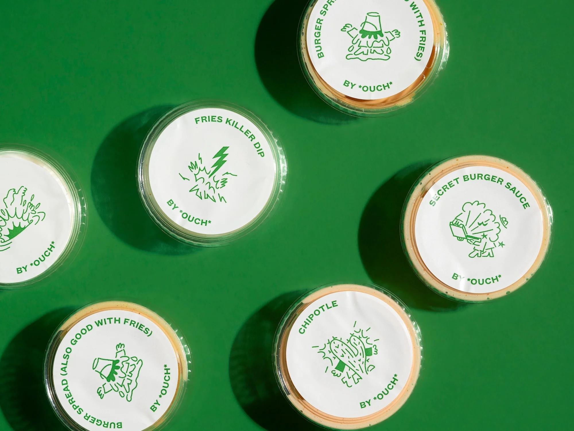 Overhead shot of assorted sauce containers with playful green illustrations and branding, set against a bright green background.