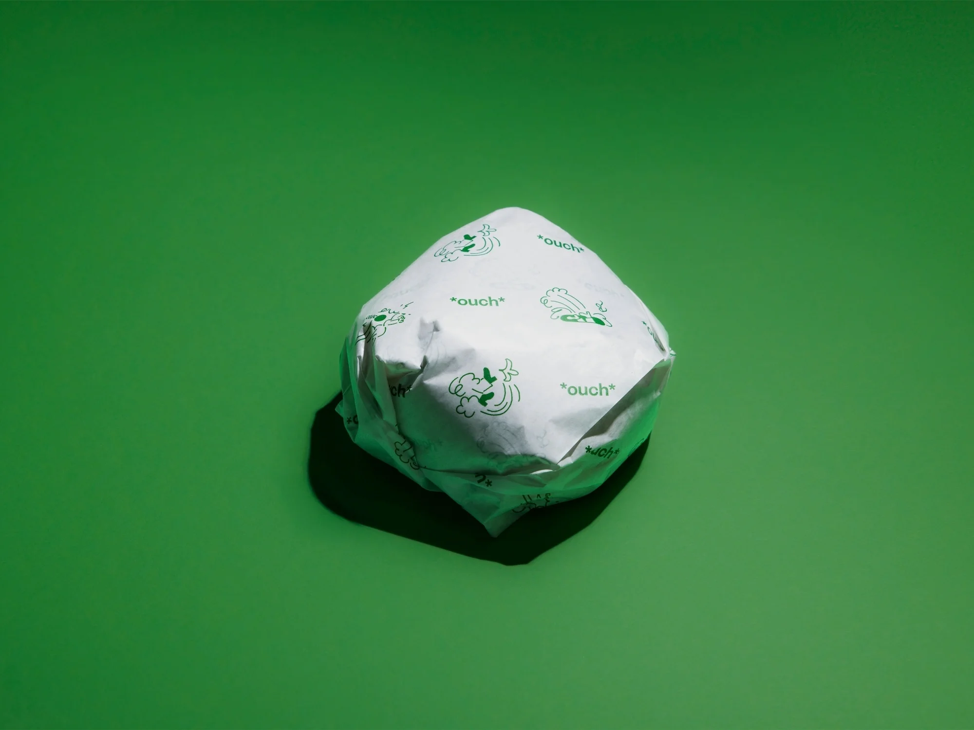 Wrapped burger on bright green background. The burger is wrapped in white paper with green text and drawings.