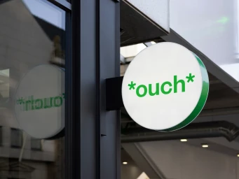 Round white illuminated sign featuring green ouch brand logo mounted on a dark building exterior