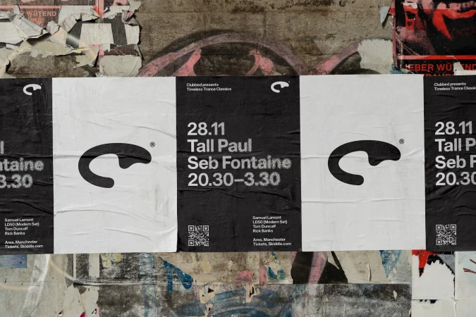 Music event posters on a concrete wall feature black and white designs with event details, logos, and QR codes for ticket information.