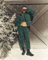 Model wearing a dark green puffer jacket and sweatpants standing outdoors in the snow