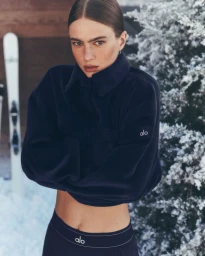 Model wearing a dark navy fleece pullover with folded arms against a snowy tree and skis