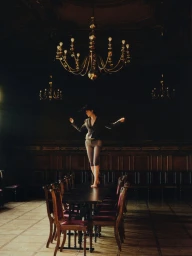 Model standing atop a long dark dining table in a grand hall beneath large ornate chandeliers, captured by Dorota Szulc for Elle Poland.